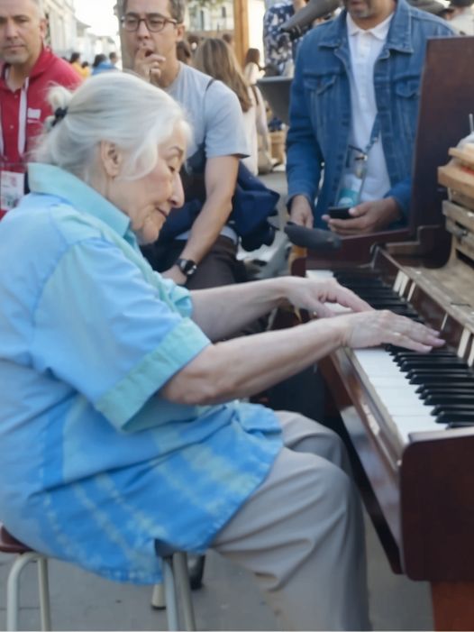 The grandmother sat in front of the piano on the street and played in such a way that people passing by gathered around her.